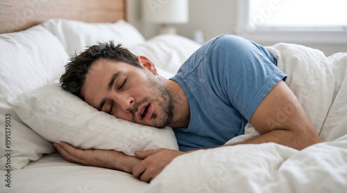 Young man sleeping soundly in a comfortable bed at home in the morning with signs of snoring or sleep apnea while resting under white sheets in a cozy bedroom