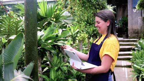 Latina woman working inside greenhouse using digital tablet for plants inventory - Small business and sustainable concept