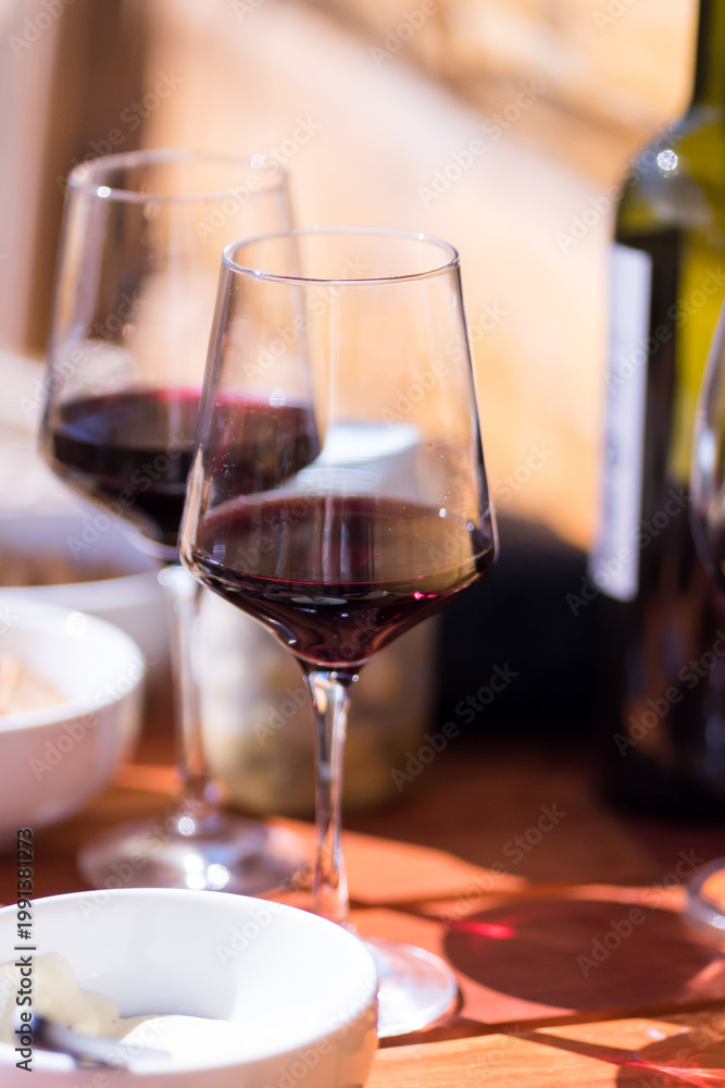 Fototapeta premium Two glasses of red wine and a bottle on a wooden table in bright sunlight
