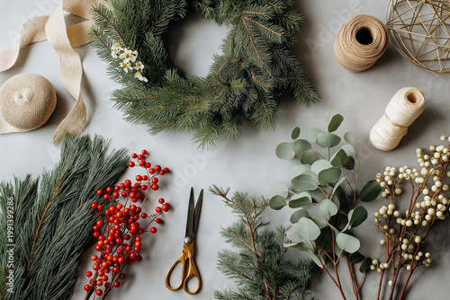 Flat lay of DIY Christmas wreath-making materials including pine branches, ribbon, scissors, berries, and wire frame on a neutral background