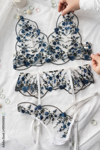 A set of delicate lace lingerie being adjusted by female hands. View from above. Film grain added to the photo.