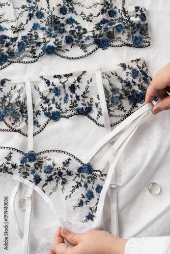 A set of delicate lace lingerie being adjusted by female hands. View from above. Film grain added to the photo.