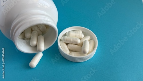 White capsules spilling out of a medicine bottle on blue background, pharmaceutical supplements and healthcare concept