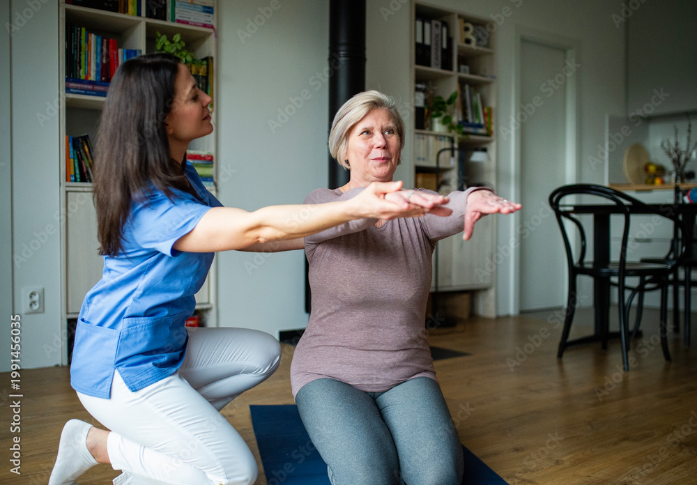 Fototapeta premium Physiotherapist helping senior woman during rehabilitation exercise at home.