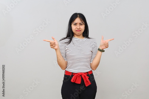 Foto A young woman stands alone on a white background pointing to the right and left hesitantly