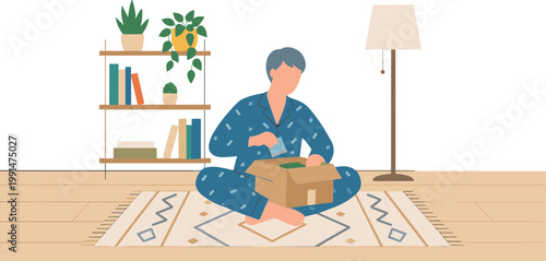 A man sits on a rug in a room unpacking a box near a bookshelf.