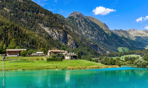 A picturesque view of small village, turquoise waters of Lake Brusson and Italian Alps