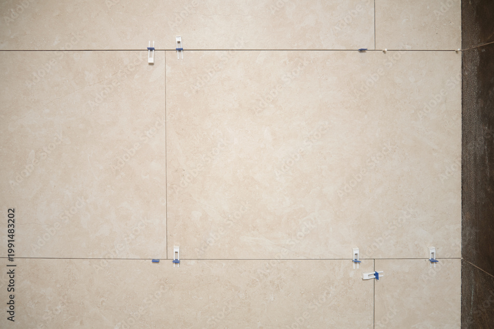Fototapeta premium Large beige porcelain wall tiles recently installed with spacers and leveling clips, showing modern construction process and precise interior wall cladding.