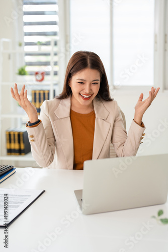 Excited office worker winner using laptop computer celebrating goal achievement. Happy young woman employee winning online getting good news in email raising hands feeling euphoric.