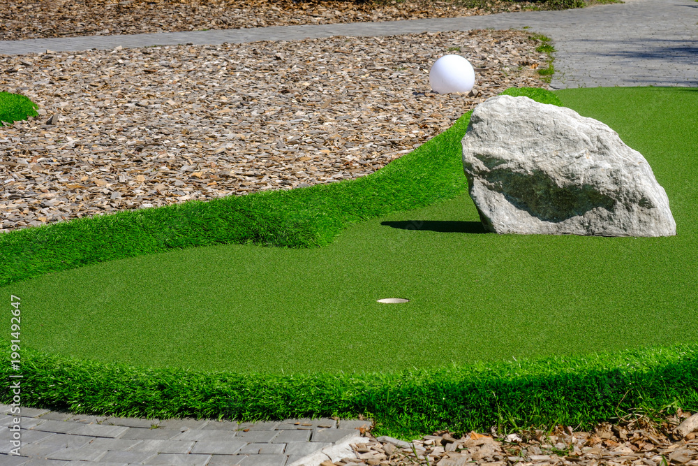 Obraz premium Mini golf course obstacle with white ball near hole
