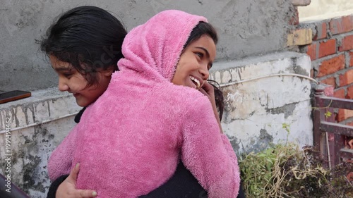 Two young Indian village girls sharing a warm hug and smiling happily on a rooftop. A candid rural lifestyle moment capturing friendship, joy, and emotional bonding in a simple village environment