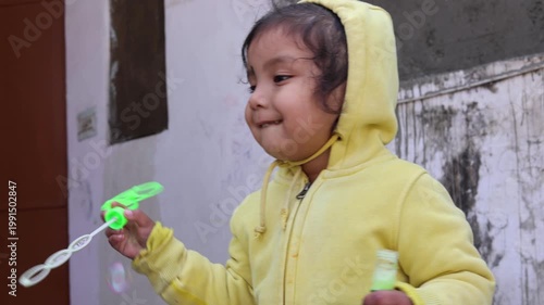 A young Indian child smiles while playing with a soap bubble toy, capturing a joyful and carefree childhood moment filled with innocence and fun in a rural village setting