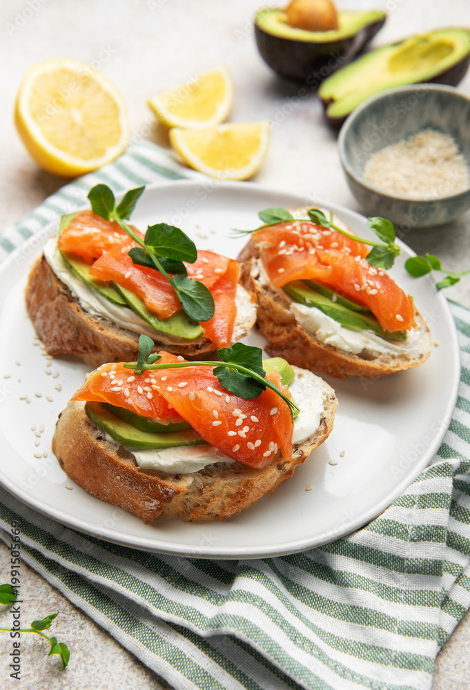 Obraz premium Preparing avocado salmon toasts with sesame seeds and lemon