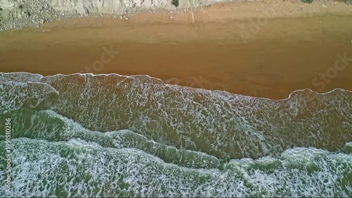 Aerial view of ocean waves gently rolling onto a sandy beach, showcasing the rhythmic movement of water and shoreline in a coastal environment