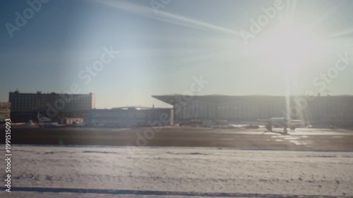 Sunlit Snowy Runway Outside Airport, Intense Low Sun Creating Strong Lens Flare, Hangar Silhouettes On Horizon, Contrail Streaks In Clear Blue Sky, Long Cold Shadows Across Tarmac, Isolated Industrial