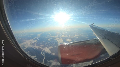 Airplane Window Sunlit Rivers And Snow, Wingtip Visible, Bright Sun Glare, Textured River Channels, Frozen Terrain Patchwork, Scratched Window Surface, Crisp Adventurous Atmosphere