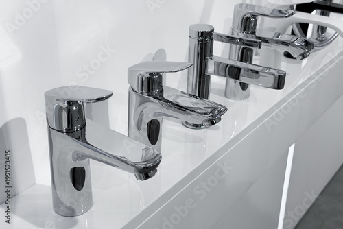 Billede på lærred Modern polished chrome bathroom sink faucets displayed on white surface