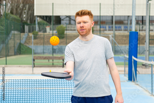 Cuadro en lienzo Man playing pickleball on outdoor court with orange ball