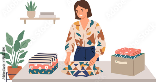 Woman folding colorful blankets on a table with plants and boxes nearby indoors.