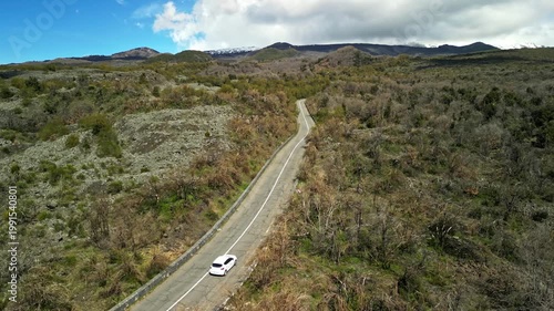 Aerial view of winding road through rocky terrain with sparse vegetation and distant mountains under a bright blue sky, showcasing natural landscape progression