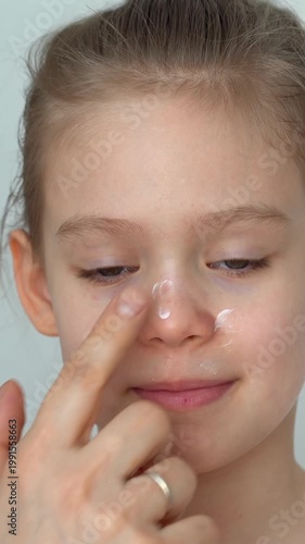 Hand applies ointment to child face with atopic dermatitis. Portrait of girls face with allergy. Diathesis. Vertical shot