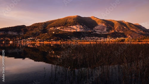 Sunset over Lake Pusiano with mountain reflection and reeds in Lombardy, Italy