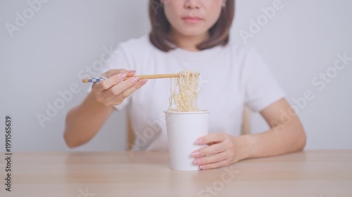Happy young Asian woman enjoying a delicious cup of hot instant noodles while relaxing at home, Cheerful female eating instant ramen with a smile at apartment. Simple lifestyle and quick meal concept