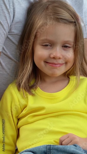 Portrait of little girl looks at camera and smiles in summer park. Happy child outdoors on picnic. Vertical shot