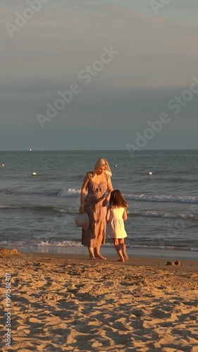 Happy family mother and daughter walk on sandy beach at sea at sunset. Summer vacation travel holiday. Vertical shot