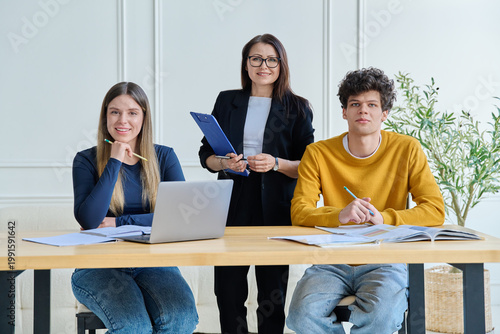 Two university students with female teacher mentor study while sitting at desk