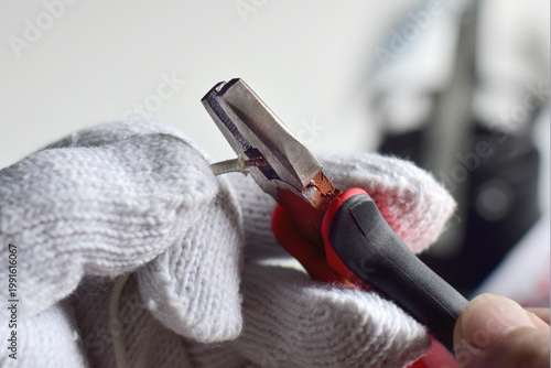 The electrician is using pliers to strip the electrical wire.