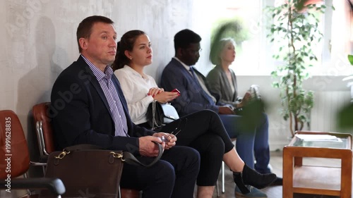 Middle-aged man sitting patiently on the bench in light waiting room of business center 