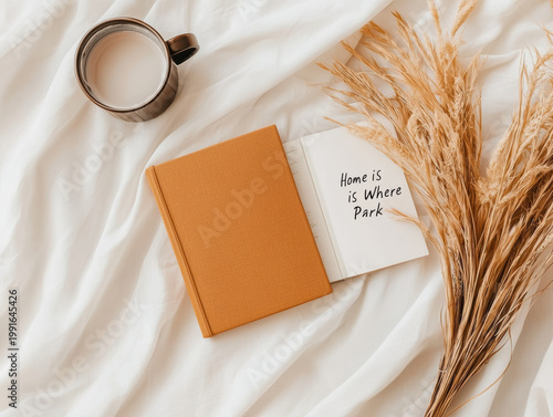  cozy scene with a cup of coffee, an open book with handwritten text, a closed notebook, and dried wheat on a soft white fabric.