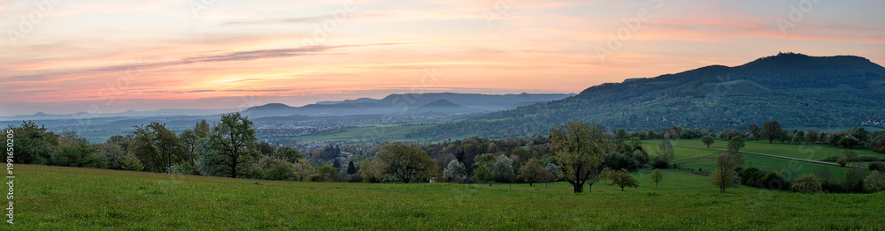 Fototapeta premium Wide panorama of Burg Teck and the Swabian Alb ridge at sunrise in spring, seen from Käppele. Dettingen unter Teck, Baden-Württemberg, Germany.