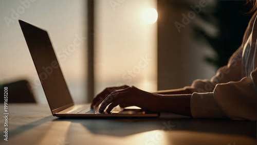 Woman typing on laptop in warm office lighting with soft background blur