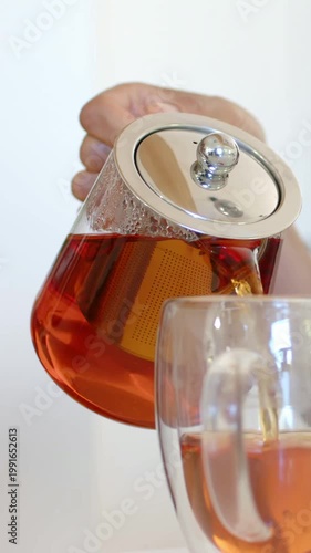 Vertical video: Tilting hand infuser pot pouring tea into mug in kitchen, filling mug, steaming
