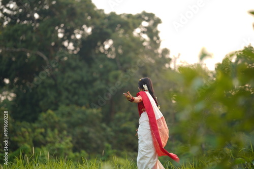 Canvas Print Woman in traditional red and white sari standing in a lush green landscape