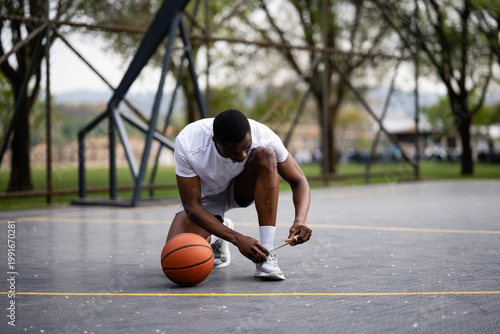 Fotografie Male basketball player tying shoelaces on outdoor court