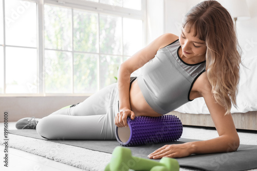 Young sporty woman training with foam roller at home