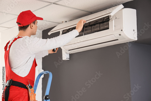 Male technician fixing air conditioner in room