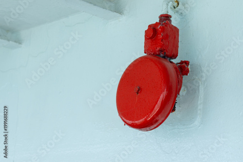 A vibrant red emergency alarm bell is mounted on a light-painted wall, commonly used on ships, in factories, and commercial buildings as a visible and reliable safety alert system.