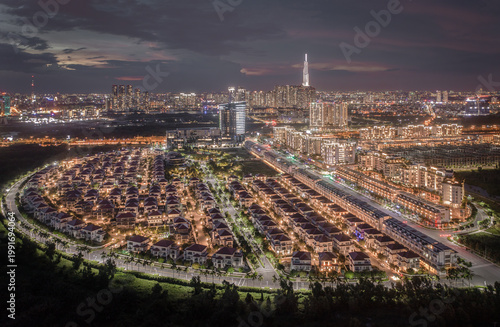 Aerial view of the city's illuminated skyline and crescent-shaped residential area, a symphony of light against the darkening sky, Ho Chi Minh City, Vietnam.