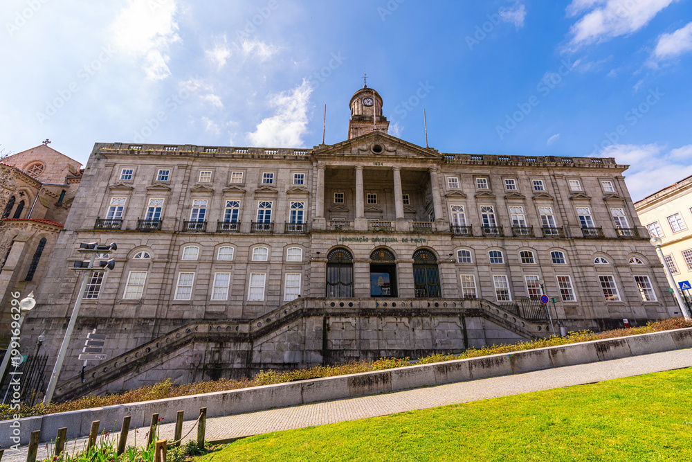 Fototapeta premium Impressive historic building of Palacio da Bolsa with clock tower and grand staircase in Porto city center. Elegant architecture, people relaxing in park and sunny European urban atmosphere.