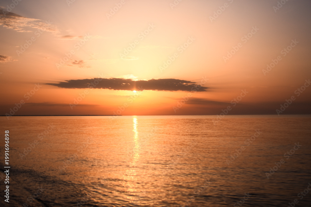 Fototapeta premium sun sets over ocean, creating radiant glow that stretches across water surface. horizon glows with soft orange and yellow tones, providing peaceful scene. stunning sunset with sun dipping into sea,