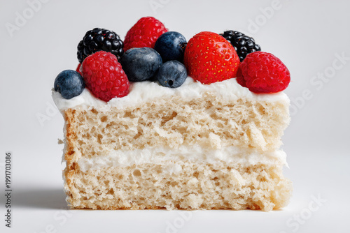 A piece of white cake with berries on a light background.