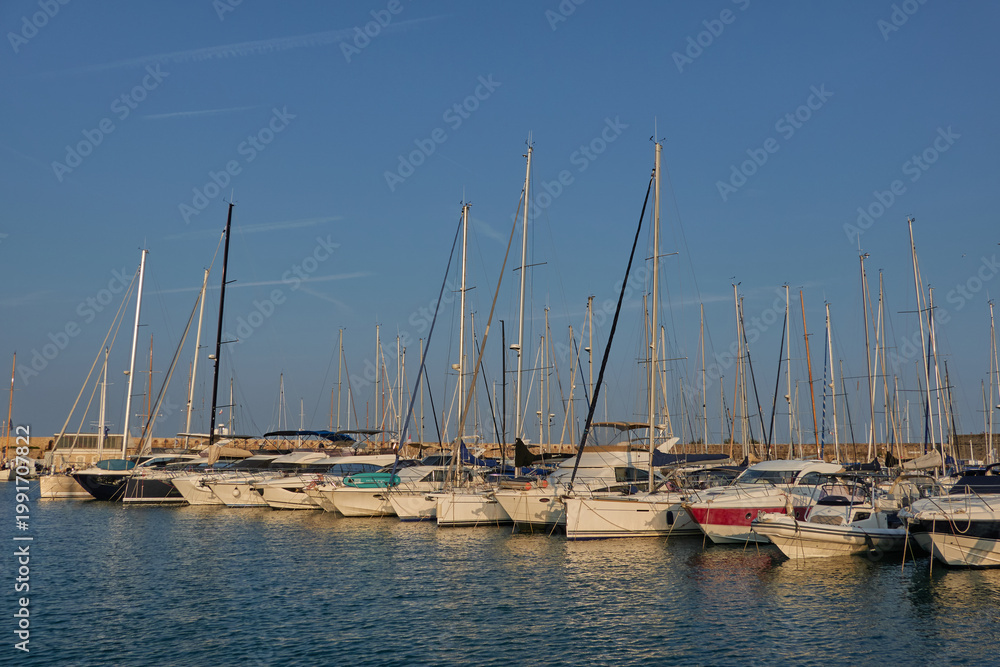 Obraz premium Antibes, France - June 8, 2025 - Many sailboats docked in a harbor under a clear blue sky with contrails