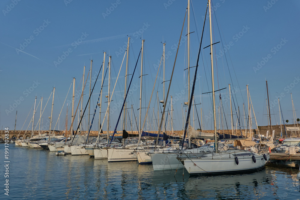 Obraz premium Antibes, France - June 8, 2025 - Many sailboats docked in a harbor under a clear blue sky with contrails