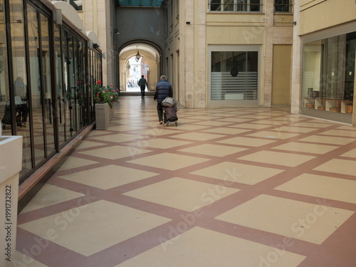 Elderly man walking with shopping trolley in a covered urban passage