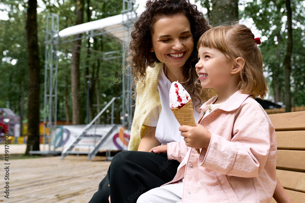 Fototapeta premium Joyful moments between a young mother and her daughter enjoying ice cream at the amusement park