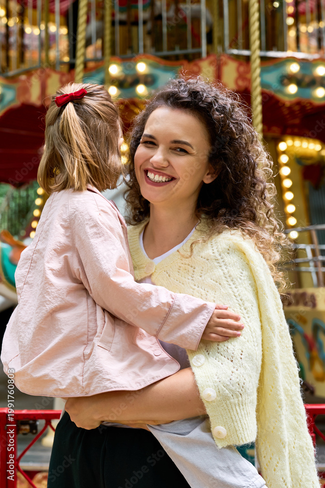 Fototapeta premium Joyful moments between a young mother and her daughter at a delightful amusement park setting